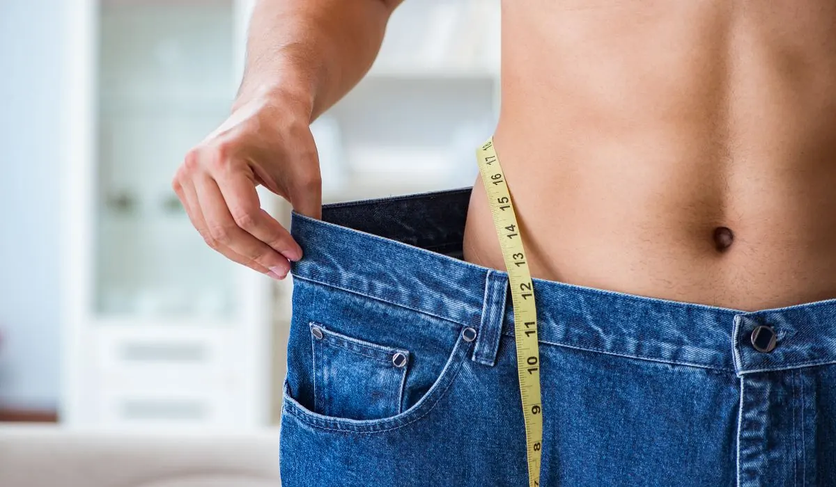 Man showing amount of weight loss by wearing his old loose jeans